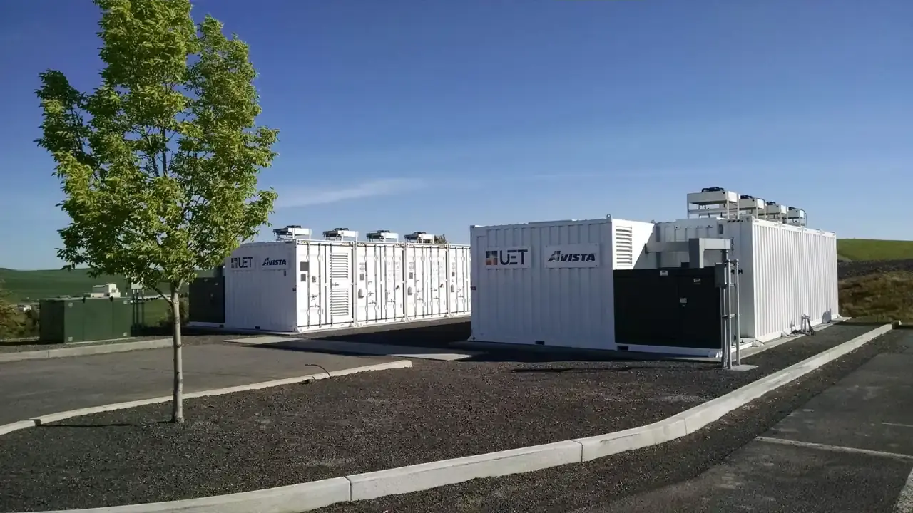White containerized battery energy storage units at an outdoor installation under a blue sky. Illustrative photo of a battery storage system, not the Bowmanville site.