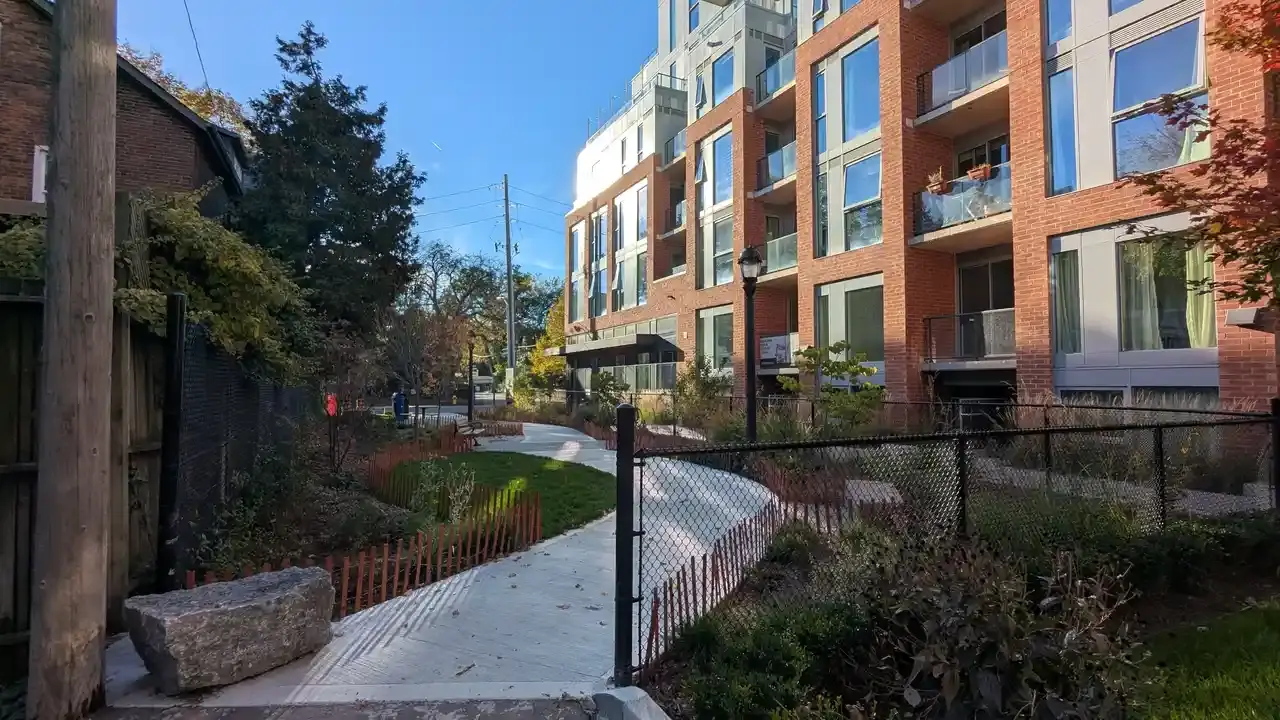 Mid-rise brick apartment building with balconies beside a small park path; no people visible.