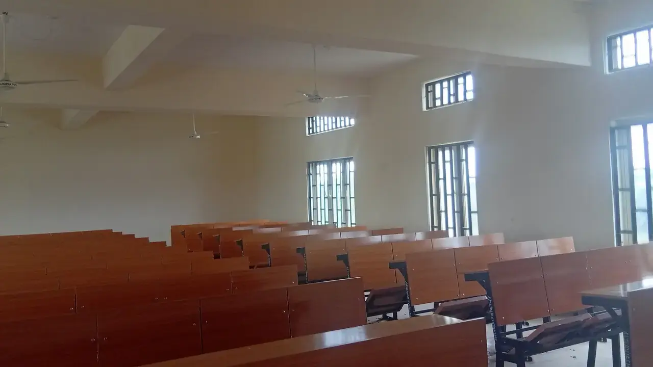 Rows of empty wooden desks in a bright, unoccupied classroom; no people visible.