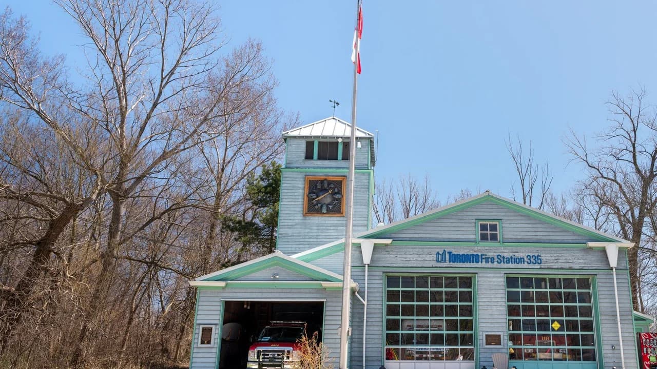 A small fire station with a red fire truck visible in the bay under a clear sky; no people visible.