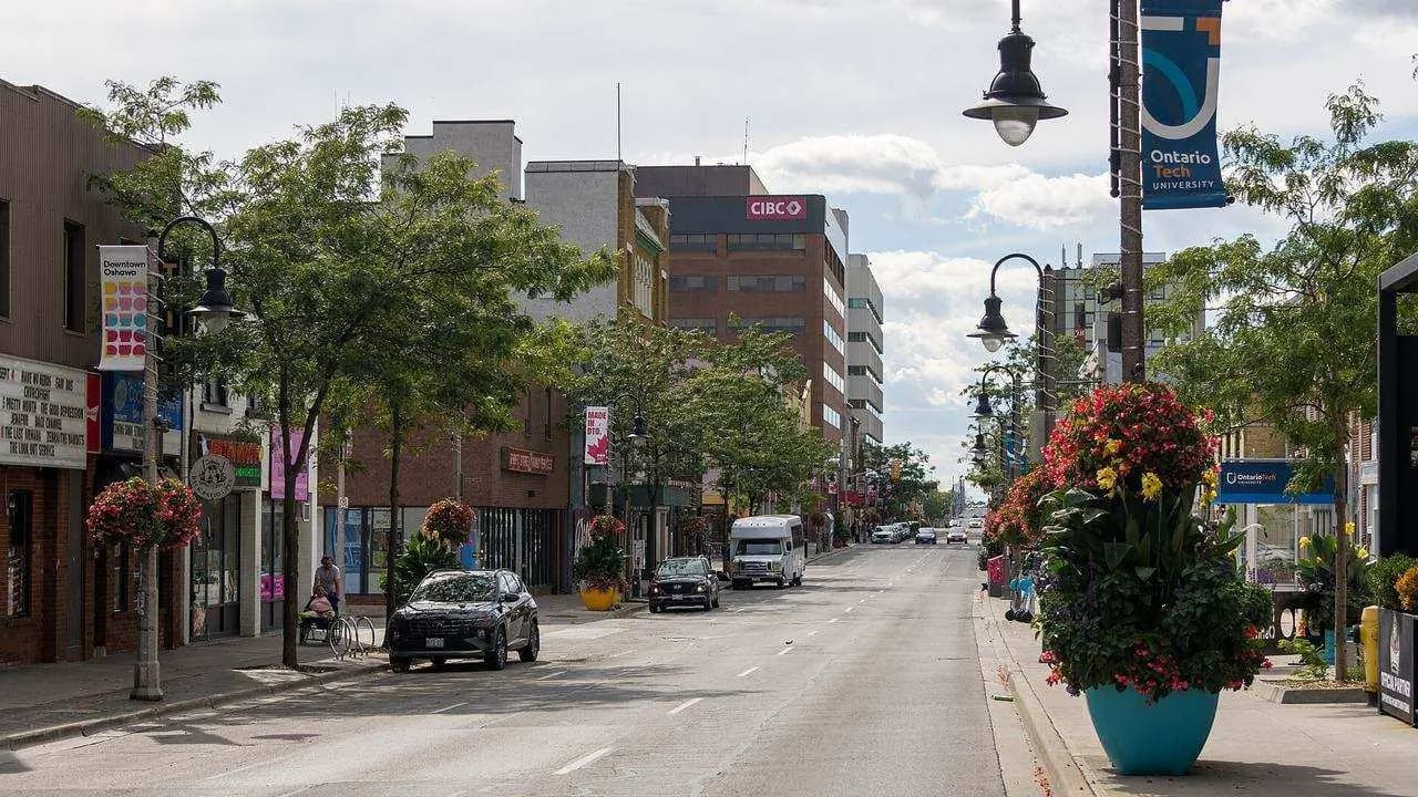 Looking west along King Street in downtown Oshawa, with storefronts, trees and flower planters; two distant people on the sidewalk are not identifiable. File photo, not the Fashion Rebel shop itself.