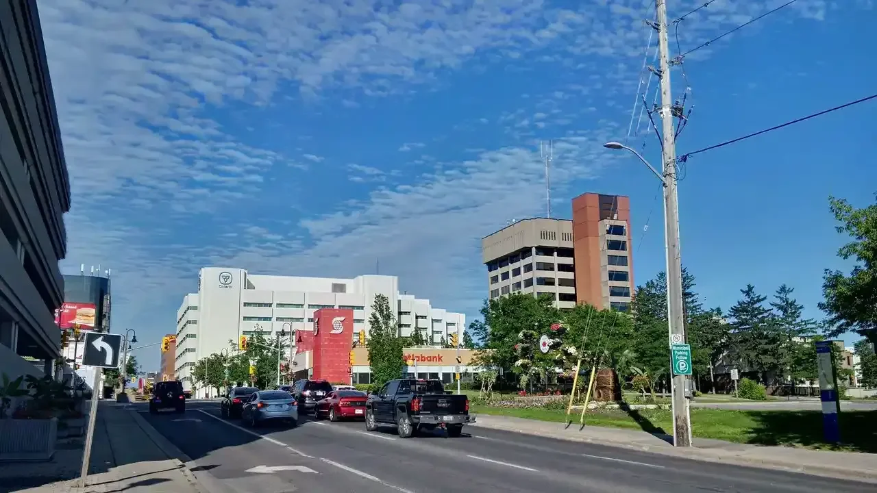 King Street in downtown Oshawa with office towers, a Scotiabank branch and cars under a blue sky.