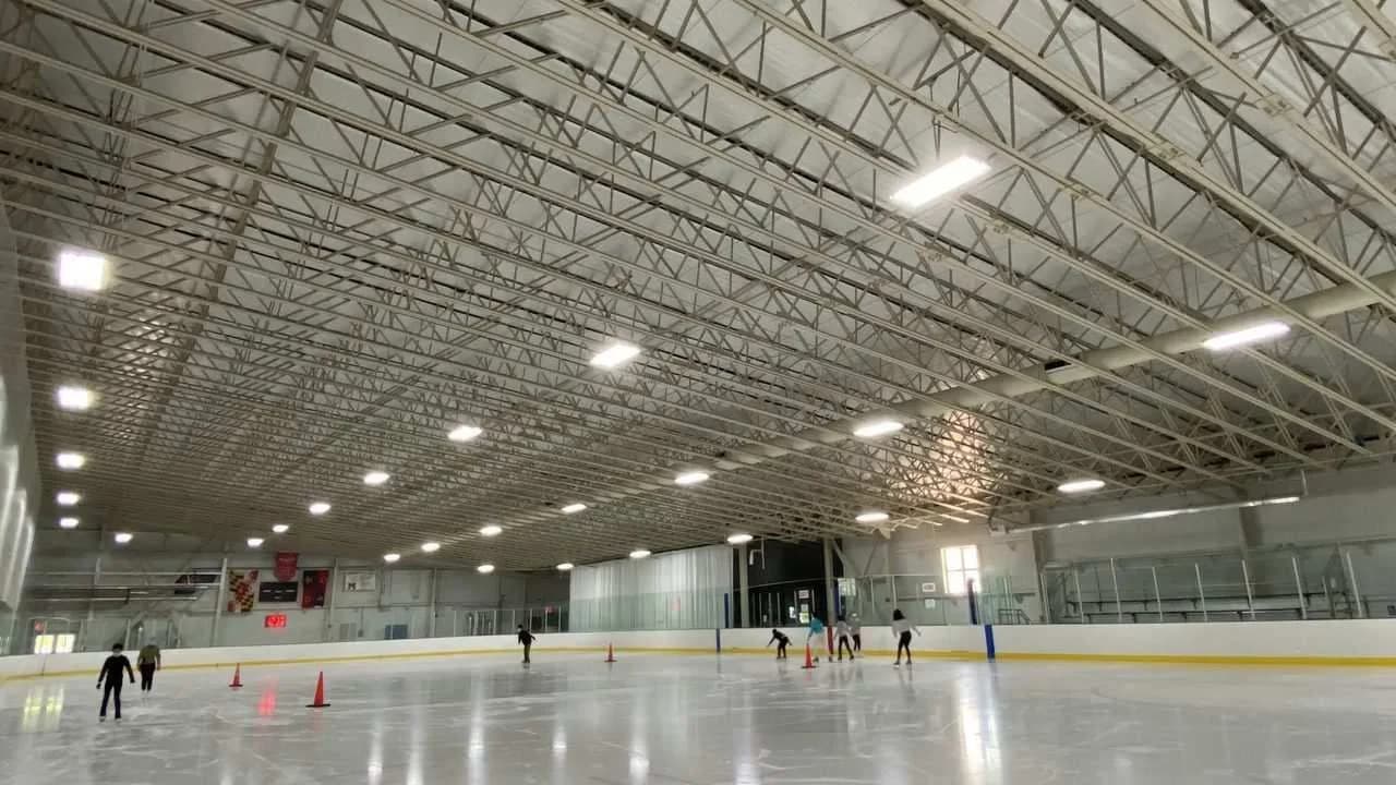 Wide view of an indoor ice rink with freshly resurfaced ice, boards, and exposed ceiling trusses