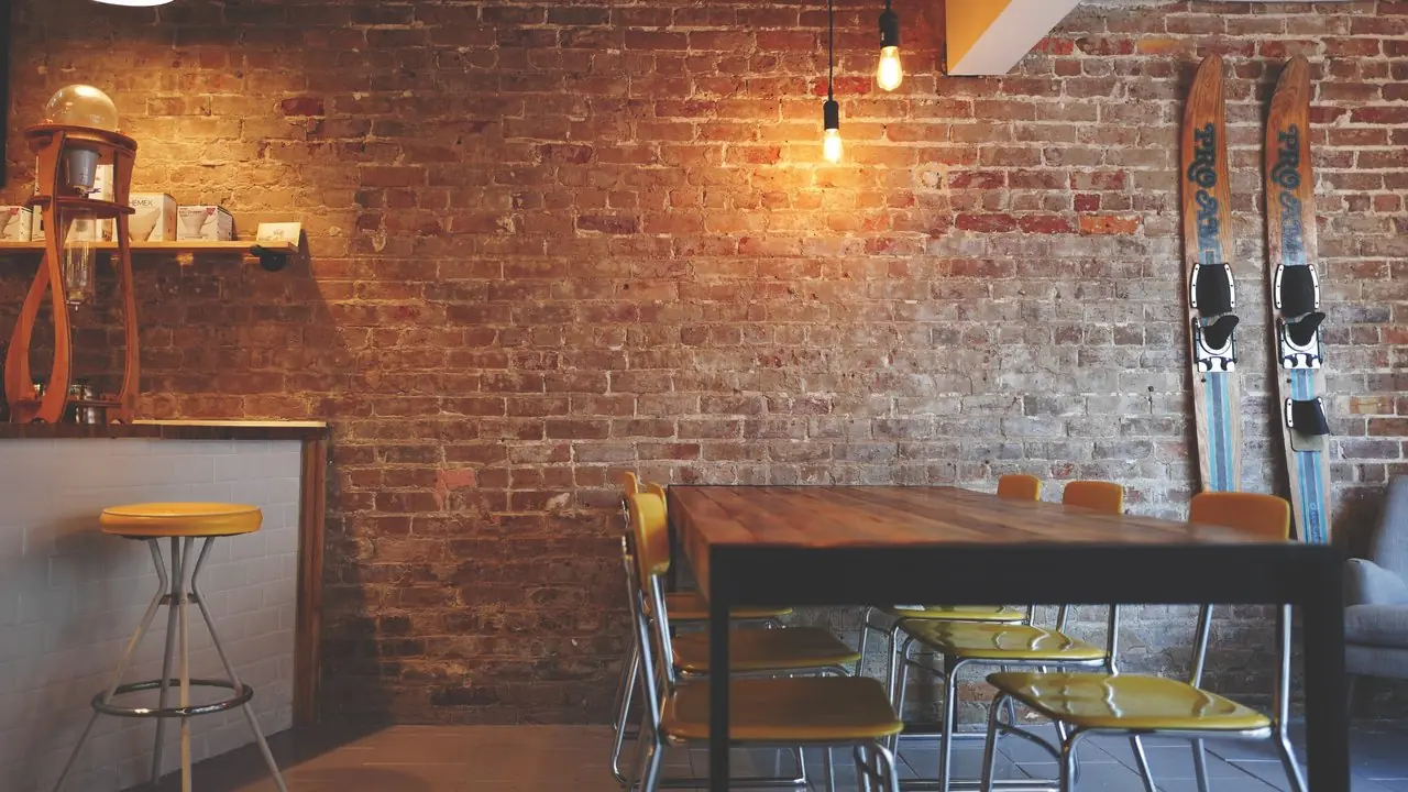 An empty, cozy coffee shop interior with a wooden table and chairs against a brick wall