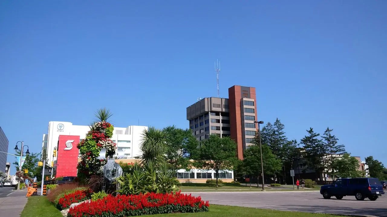 Oshawa City Hall on a clear summer day, with its brick tower, trees, landscaped lawn and red flower bed in the foreground; no identifiable people visible.