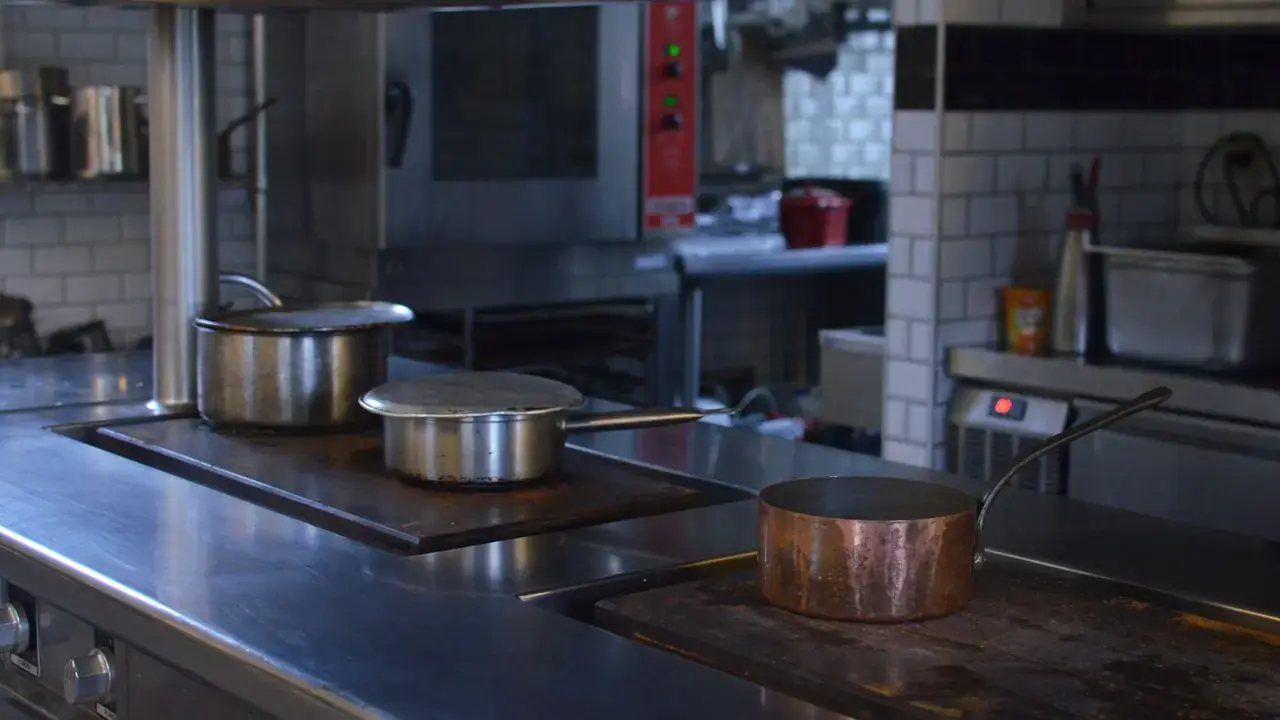 Stainless steel pots and a copper pan on counters in an empty professional kitchen; no people visible.