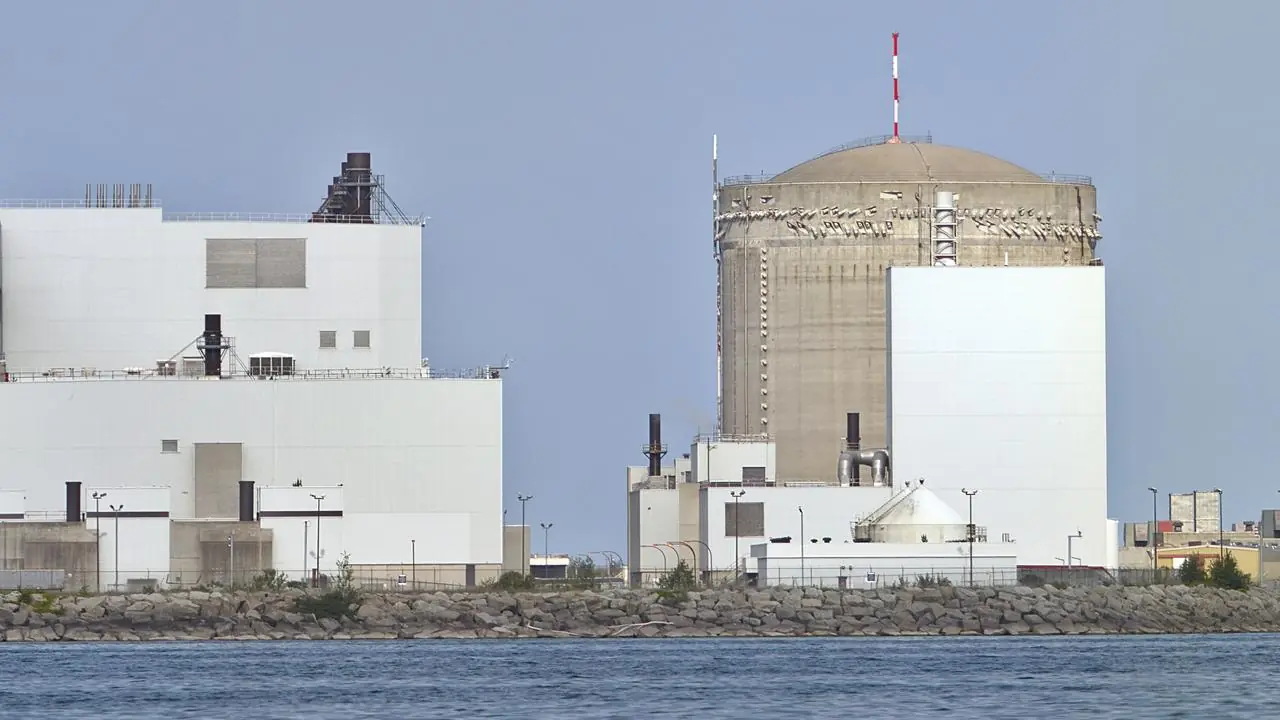 The Darlington Nuclear Generating Station viewed from across the water, with its white plant buildings and domed reactor building on the shoreline; no people visible.