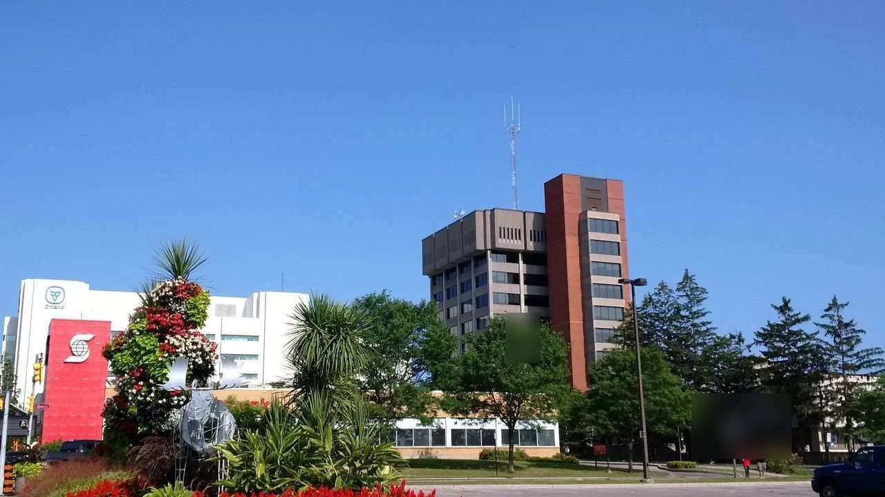 Daytime exterior view of Oshawa City Hall towers with the landscaped forecourt garden under a clear blue sky.