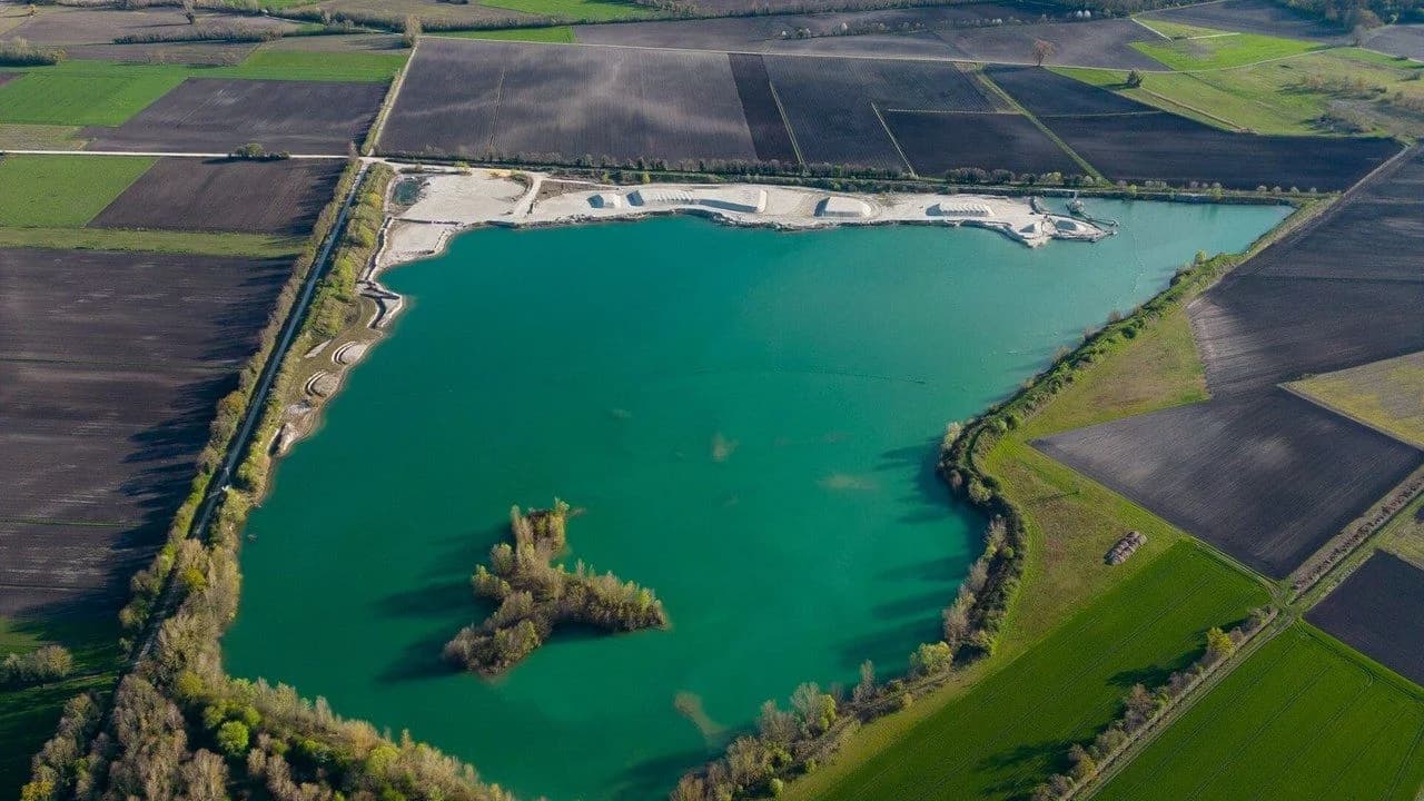 Aerial view of a pond with turquoise water surrounded by farmland; no people visible