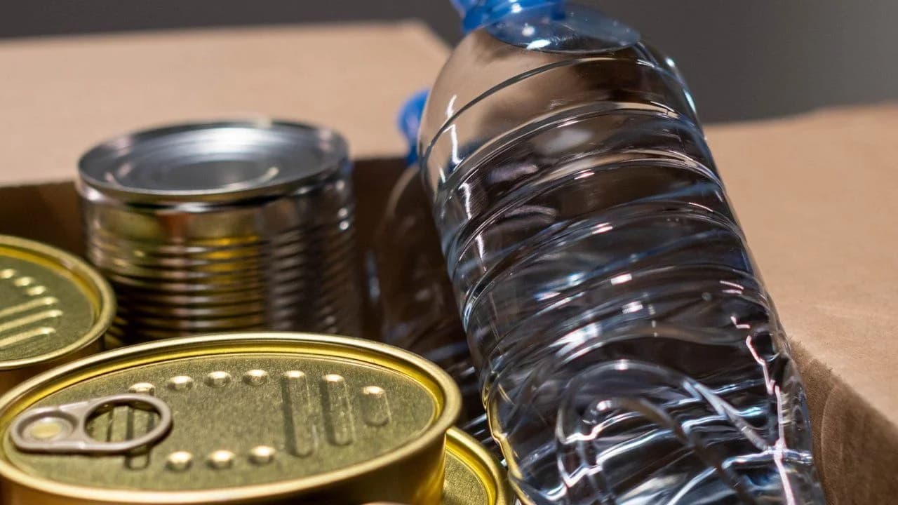 Canned goods and a plastic water bottle packed in a cardboard box of food donations.