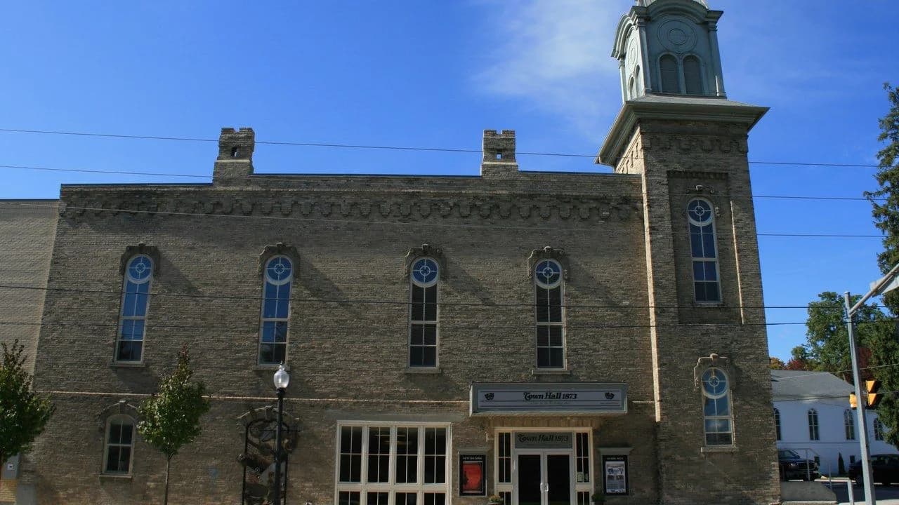 The historic former Port Perry Town Hall at 302 Queen Street in Scugog, Ontario: a brick heritage building with a clock tower under a clear blue sky; no people visible.