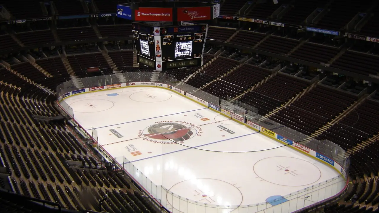 An empty ice hockey arena with the rink and surrounding stands under the lights; no people visible.