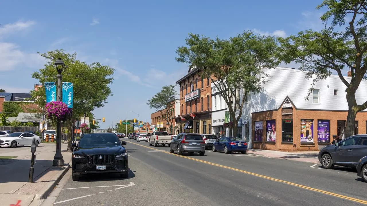 Looking north along Brock Street in downtown Whitby, Ontario, with parked cars, heritage storefronts and trees; no people in frame