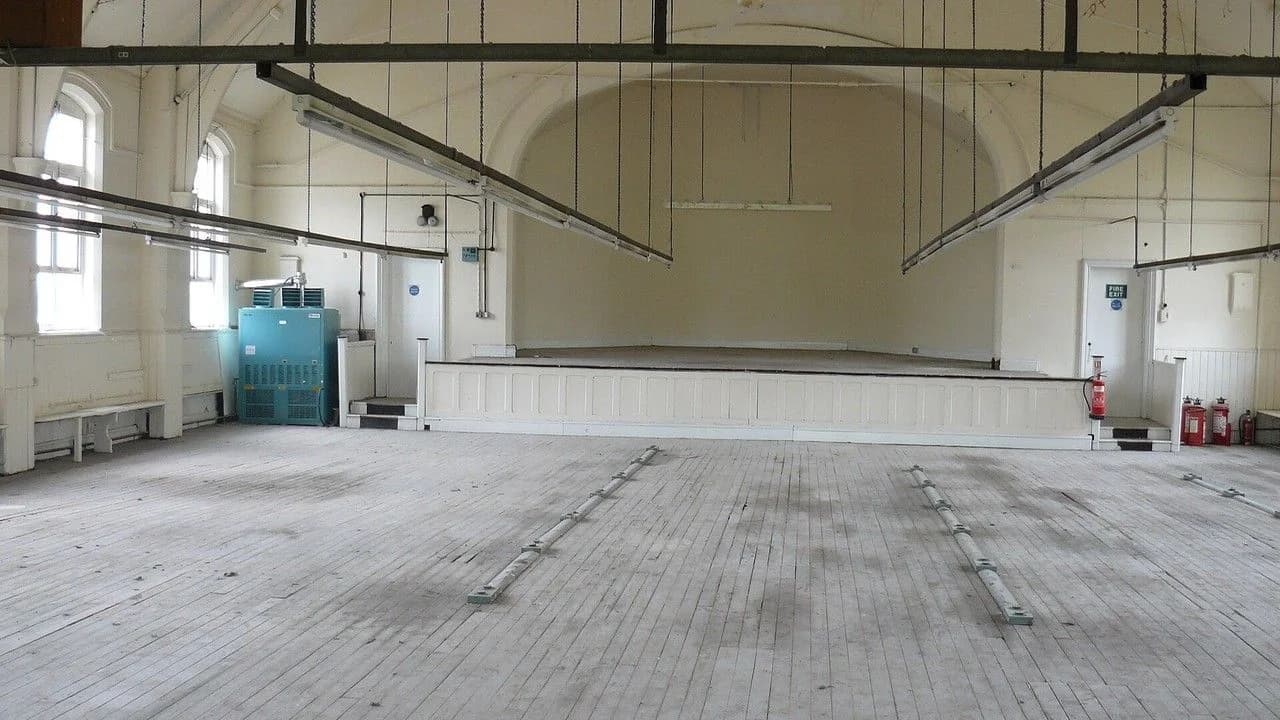 Empty community dance hall interior with wooden floor and stage; no people.