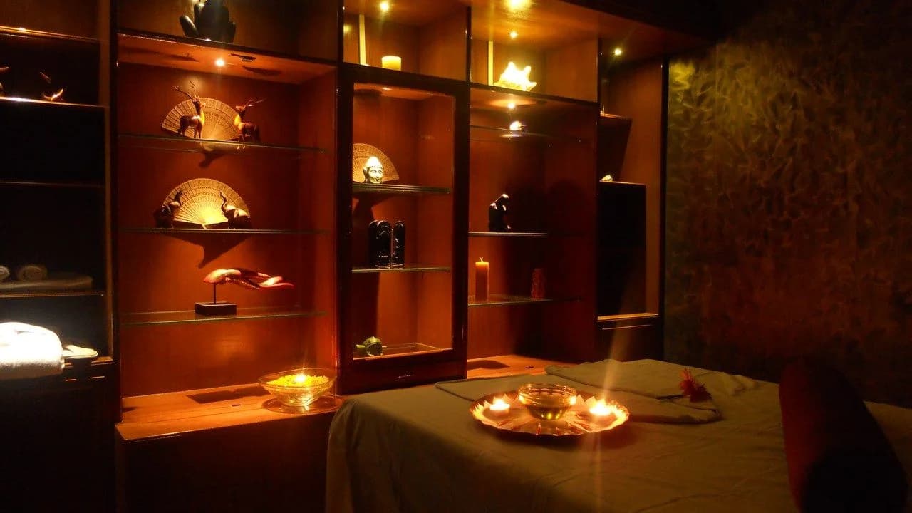 A candlelit spa treatment room with a prepared massage bed, lit candles and wooden display shelves