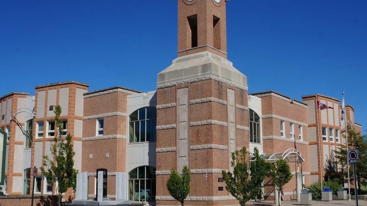 Exterior of a brick Ontario town hall with a clock tower under a clear blue sky; no people visible