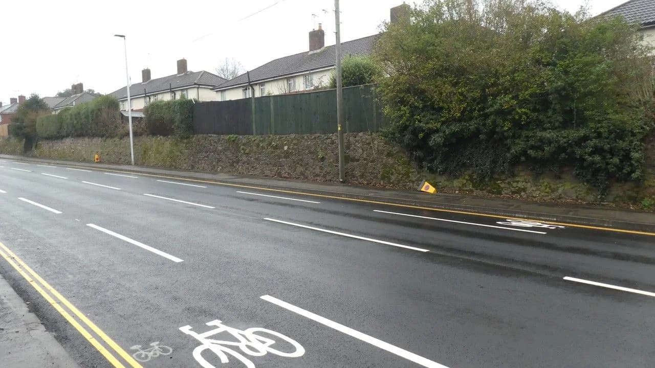 A newly marked on-road bicycle lane with freshly painted white bicycle symbols on wet asphalt; no people