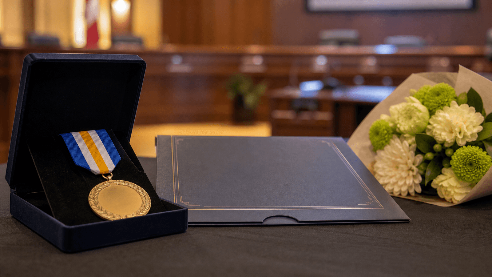 Photorealistic editorial image of an award medal, certificate folder, and bouquet in a civic hall.